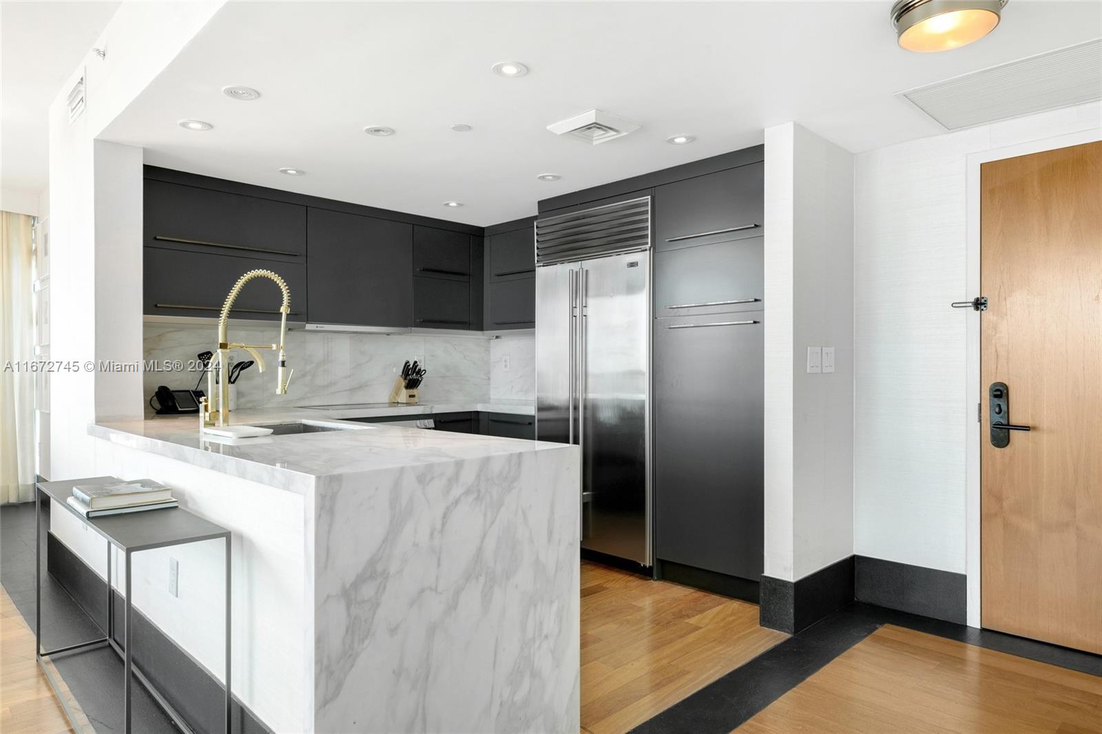 A modern kitchen features dark cabinetry, a marble waterfall island, and stainless steel appliances — 101 20th St # 2706, Miami Beach FL 33139, MIAMI BEACH, FL