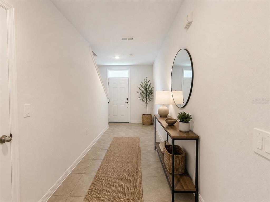 A bright entryway features tile flooring, a console table, a round mirror, and a staircase — 35710 KINSEY POINT, ZEPHYRHILLS, FL