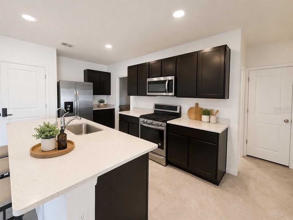 A kitchen features dark cabinets, stainless steel appliances, and a white quartz island countertop — 35710 KINSEY POINT, ZEPHYRHILLS, FL