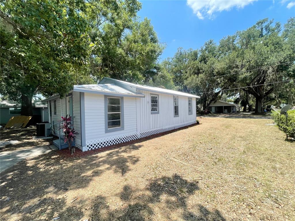 A white mobile home with a metal roof sits on a grassy lot with trees — 630 N NASHUA AVENUE, FORT MEADE, FL