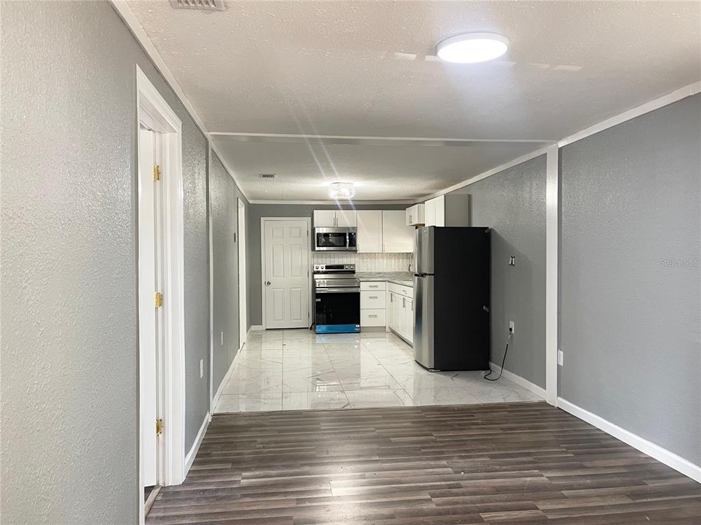 A kitchen with white cabinets and stainless steel appliances transitions to a wood-floored living area — 630 N NASHUA AVENUE, FORT MEADE, FL