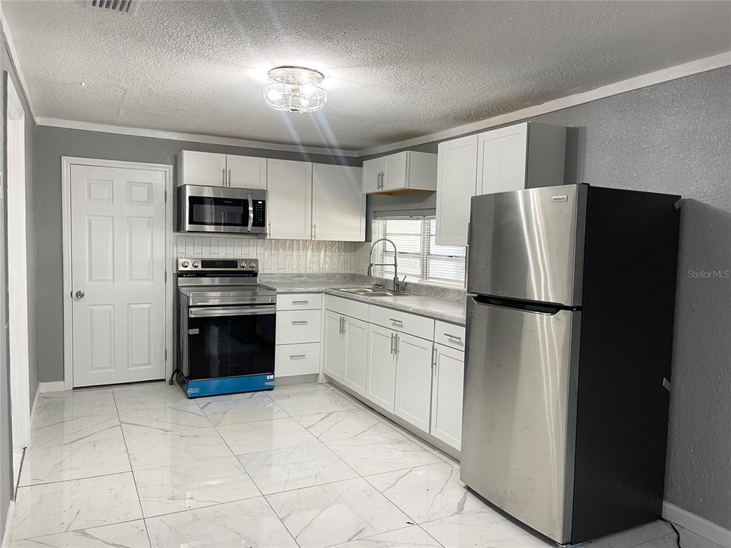 A kitchen features white cabinets, stainless steel appliances, a tiled backsplash, and white marble-look flooring — 630 N NASHUA AVENUE, FORT MEADE, FL
