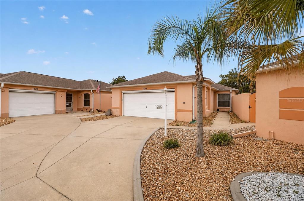 A view of two adjacent single-story stucco houses with attached garages and gravel landscaping — 1630 TAMPICO PLACE, LADY LAKE, FL