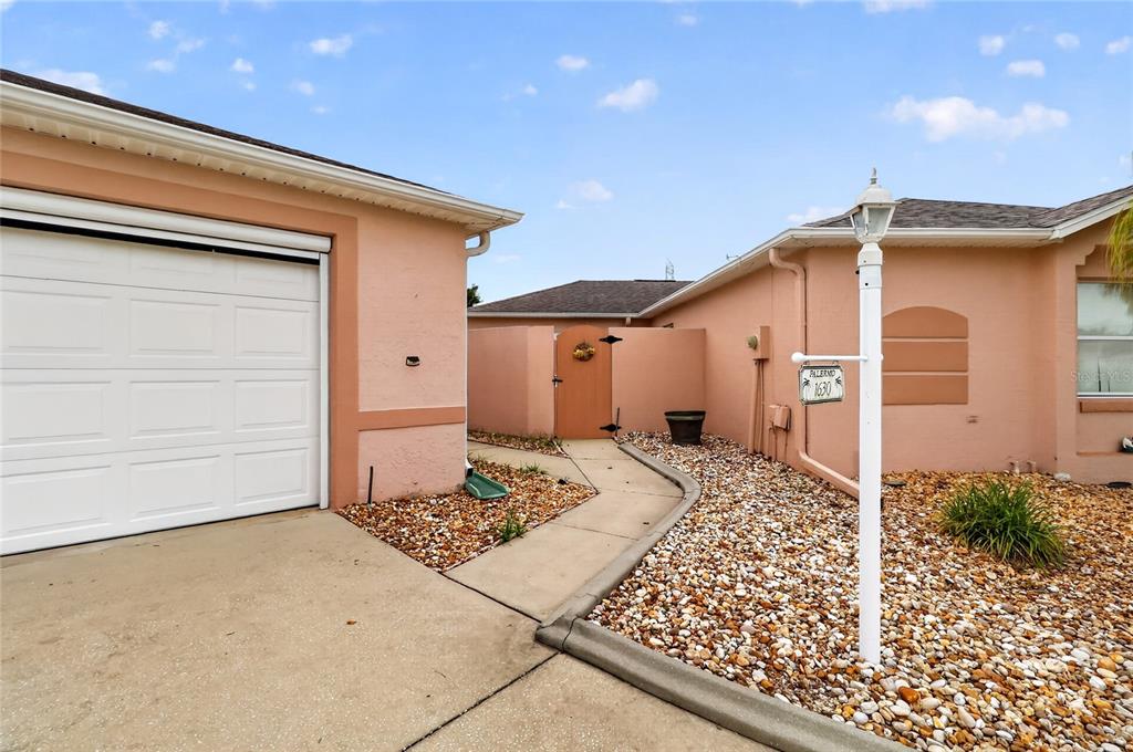 A peach-colored house exterior features a white garage door, a walkway, and a gravel yard — 1630 TAMPICO PLACE, LADY LAKE, FL