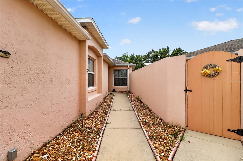 A concrete walkway leads between a peach-colored house wall and a matching privacy gate — 1630 TAMPICO PLACE, LADY LAKE, FL