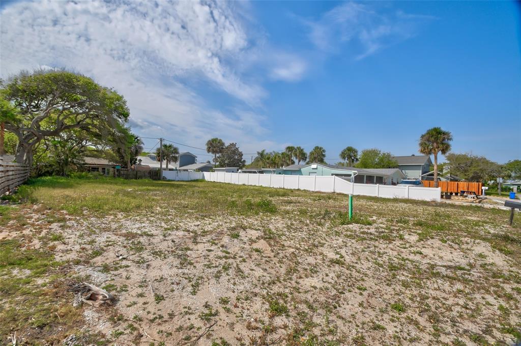 A vacant, sandy residential lot is enclosed by a white vinyl fence under a blue sky — 209 NORMANDY AVENUE, NEW SMYRNA BEACH, FL