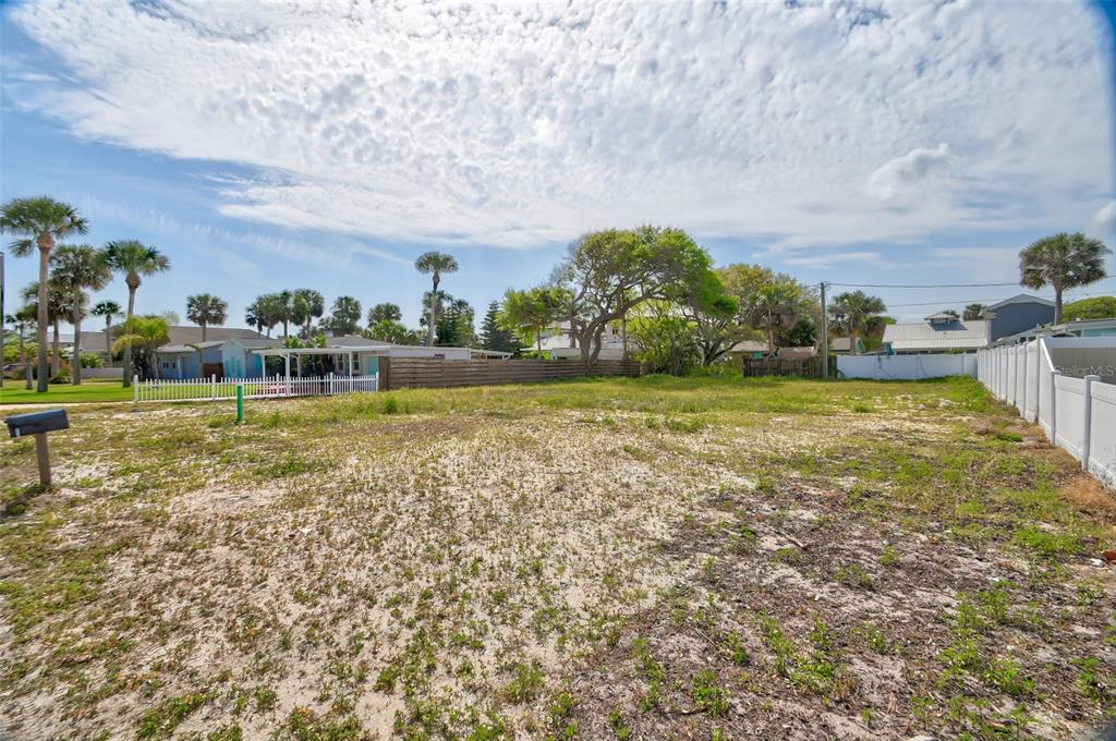 A vacant, sandy residential lot is enclosed by white and wooden fences under a cloudy sky — 209 NORMANDY AVENUE, NEW SMYRNA BEACH, FL