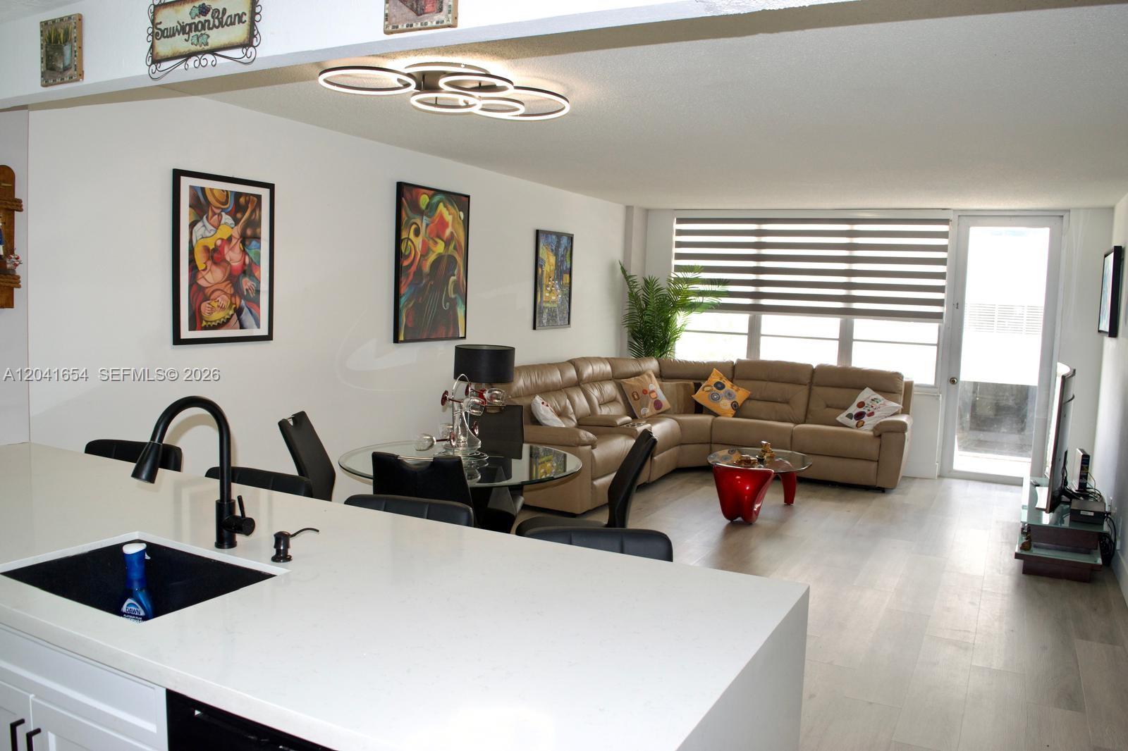An open-concept living and dining area features a sectional sofa, glass tables, and kitchen island — 3725 S Ocean Dr # 423, Hollywood FL 33019, HOLLYWOOD, FL