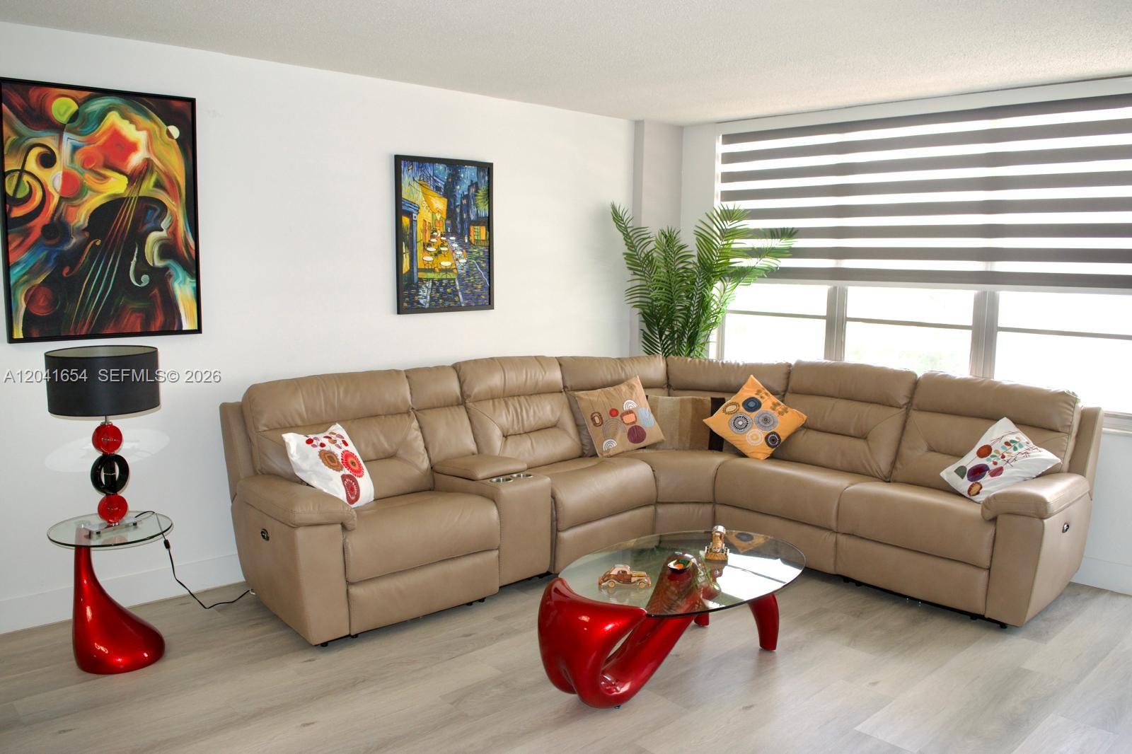 A living room features a beige sectional sofa, a red coffee table, and abstract wall art — 3725 S Ocean Dr # 423, Hollywood FL 33019, HOLLYWOOD, FL