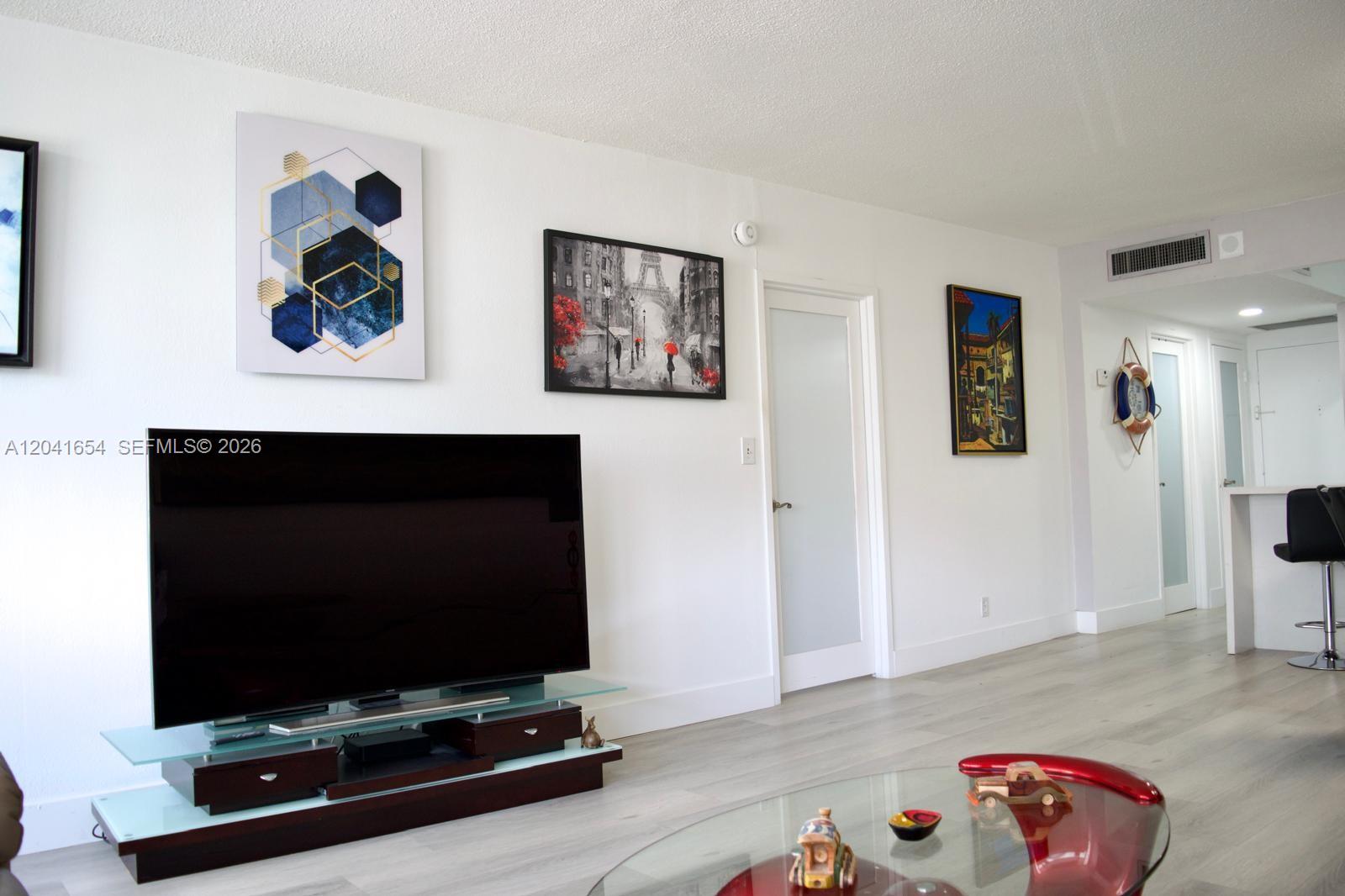 A living room features a television on a glass stand, wall art, and light flooring — 3725 S Ocean Dr # 423, Hollywood FL 33019, HOLLYWOOD, FL