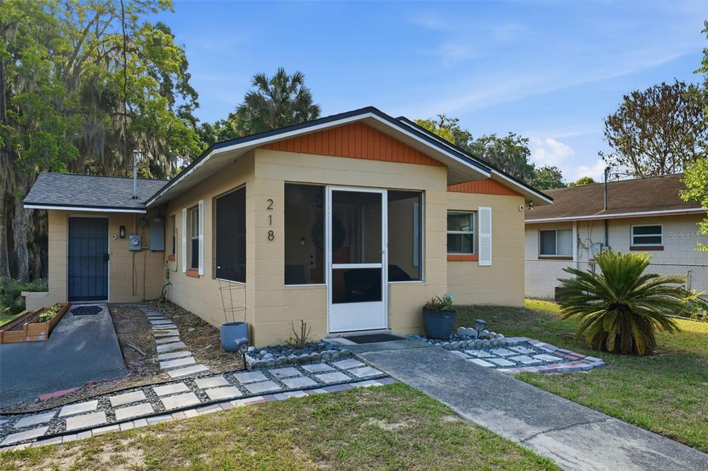 A single-story tan house with a screened-in front porch and a paved walkway — 218 S EAST STREET, LEESBURG, FL