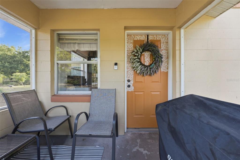 A covered porch features two chairs, a grill, and an orange door with a wreath — 218 S EAST STREET, LEESBURG, FL