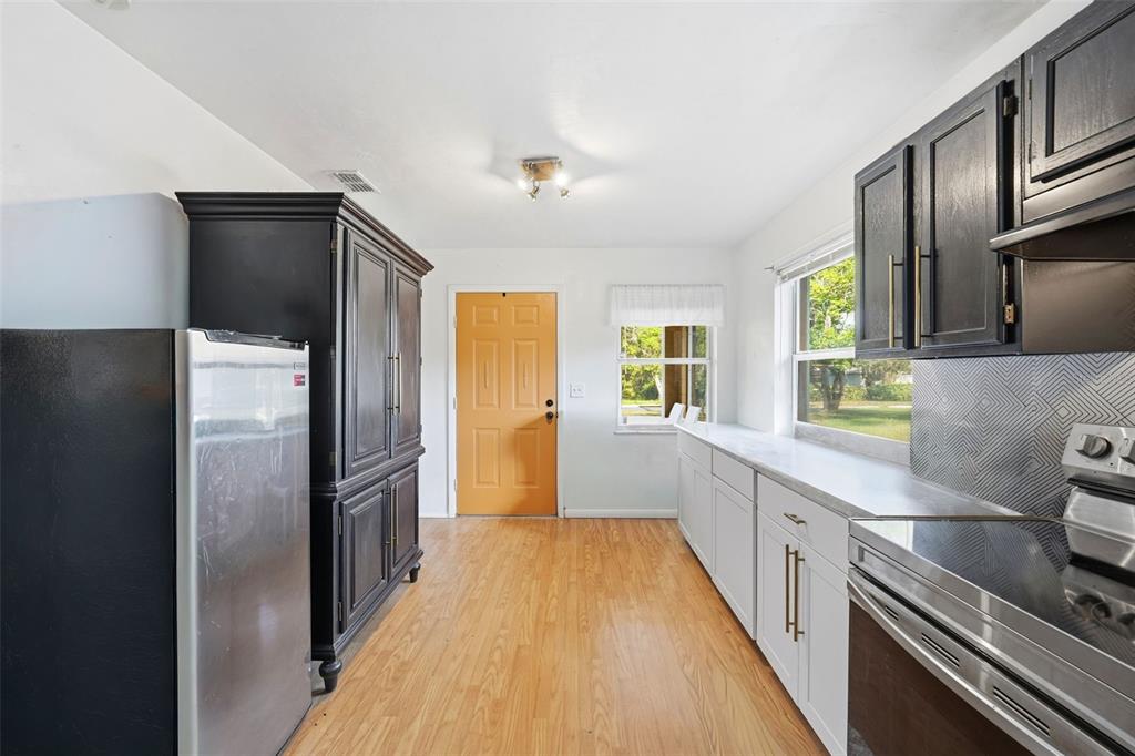 A kitchen features white lower cabinets, black upper cabinets, stainless steel appliances, and a yellow door — 218 S EAST STREET, LEESBURG, FL