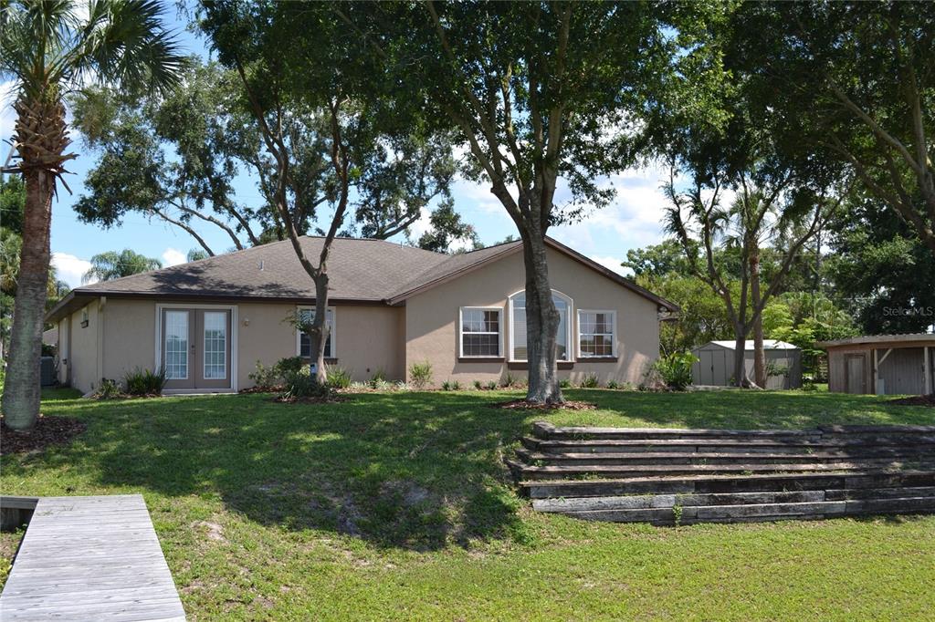 A tan house with a wooden deck and tiered retaining wall sits on a grassy lot — 26 SE OCALE WAY, SUMMERFIELD, FL
