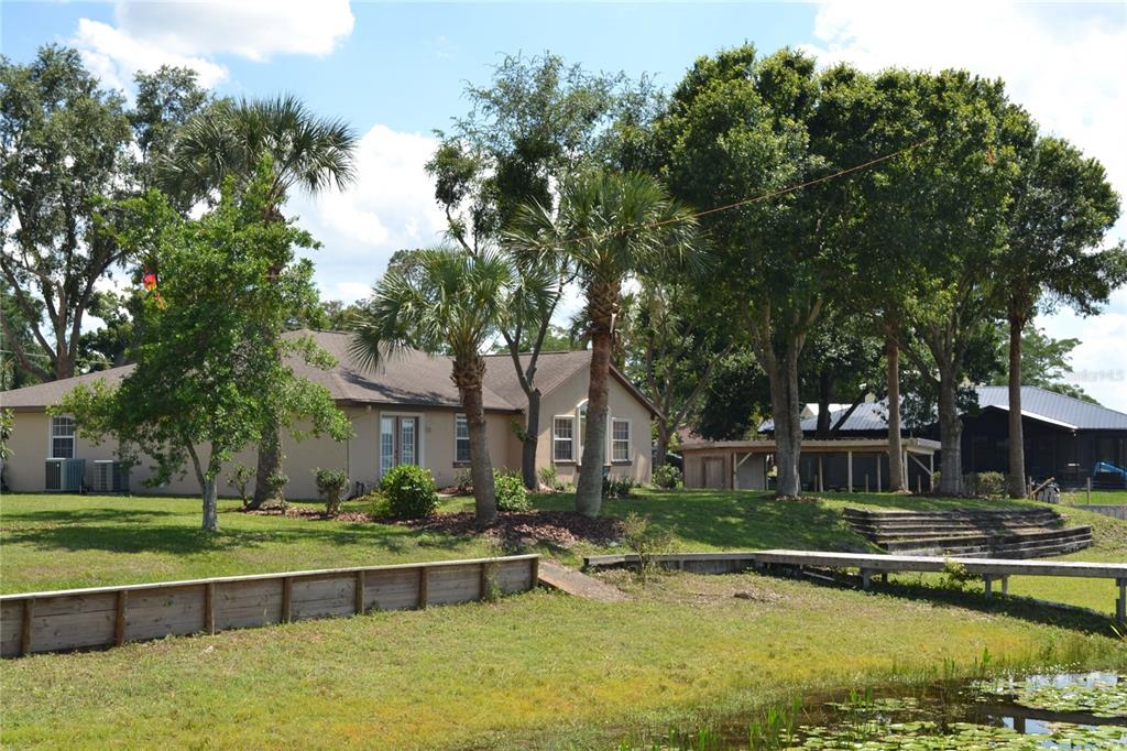 A tan house with a wooden bulkhead and dock sits beside a small pond — 26 SE OCALE WAY, SUMMERFIELD, FL
