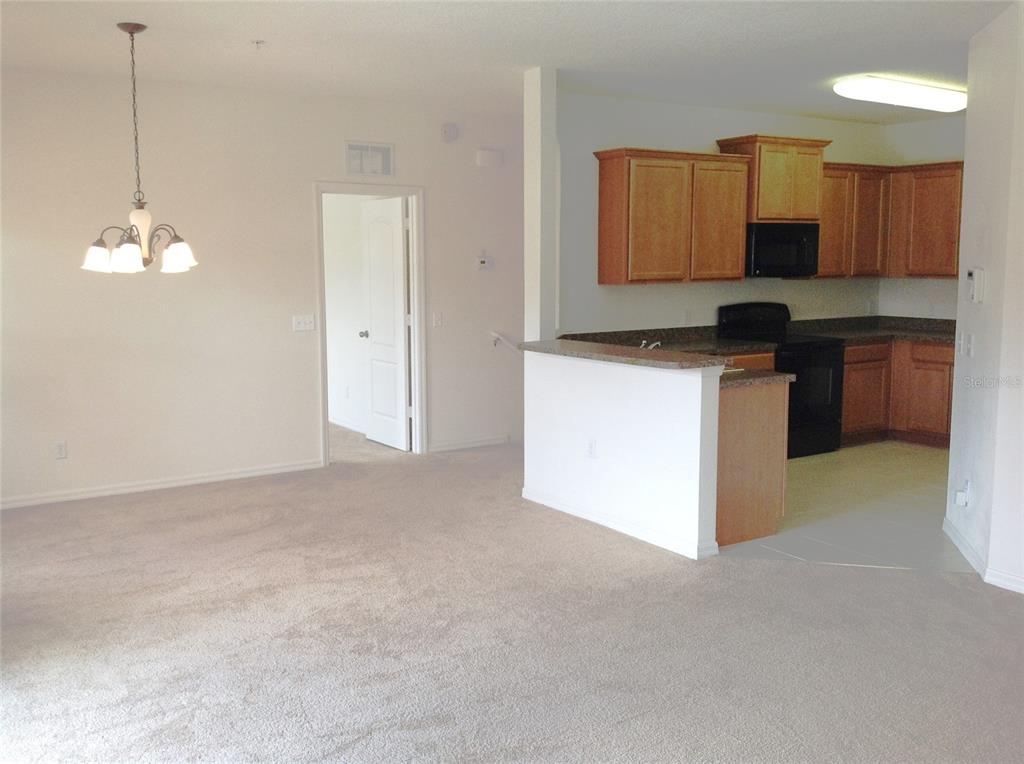 An open-concept living area features beige carpeting, a dining light fixture, and a kitchen — 2300 BETSY ROSS LANE, ST CLOUD, FL