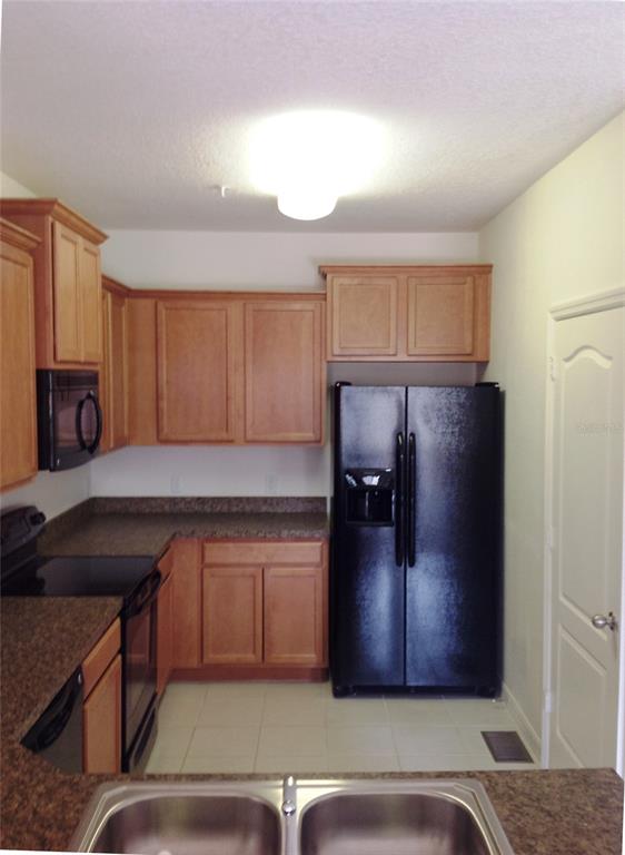 A kitchen features light wood cabinets, dark countertops, black appliances, and a double sink — 2300 BETSY ROSS LANE, ST CLOUD, FL