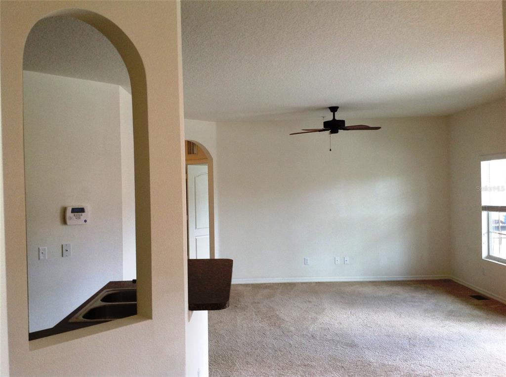 A carpeted living room features a ceiling fan and an arched pass-through to the kitchen — 2300 BETSY ROSS LANE, ST CLOUD, FL