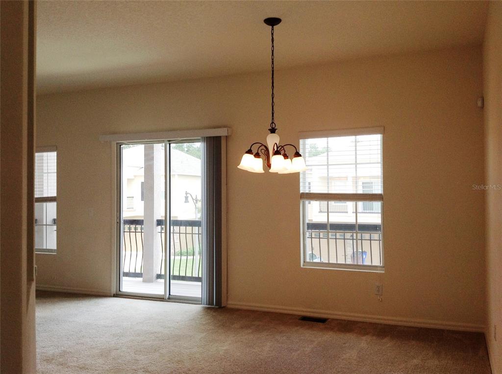 A dining area with beige carpet, a hanging chandelier, sliding glass doors, and two windows — 2300 BETSY ROSS LANE, ST CLOUD, FL