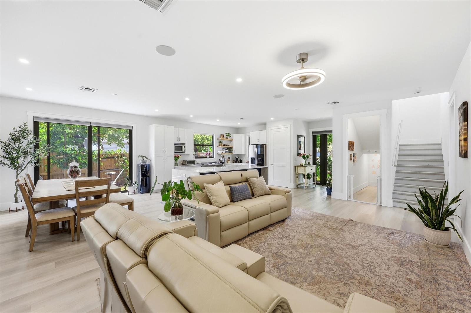 An open-concept living room and kitchen feature light wood floors, beige sofas, and a staircase — 740 Winters Street, West Palm Beach FL 33405, WEST PALM BEACH, FL