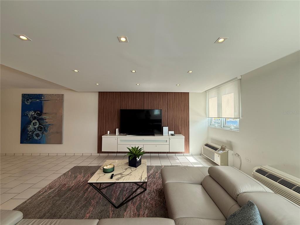 A living room features a wood-paneled accent wall, a white media console, and tile flooring — 5245 ISLA VERDE AVENUE UNIT 208, CAROLINA, PR