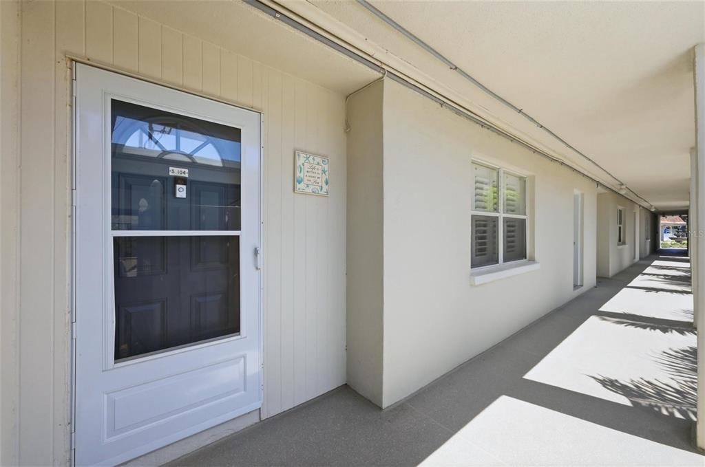 A white door with a screen and a window are visible along a covered walkway — 2110 BENJAMIN FRANKLIN DRIVE UNIT 104, SARASOTA, FL