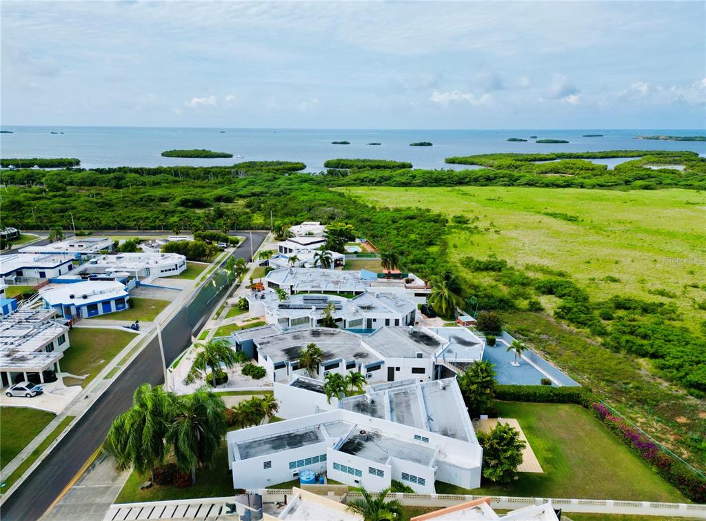 An aerial view shows a cluster of white buildings surrounded by green vegetation and water — . VILLAS DE BAHIA UNIT D-7, LAJAS, PR