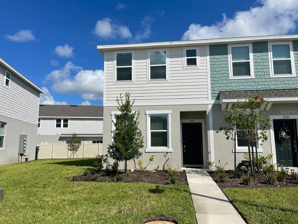 A two-story townhouse with a light-colored stucco and siding exterior under a blue sky — 3335 COMPOSITION STREET, KISSIMMEE, FL