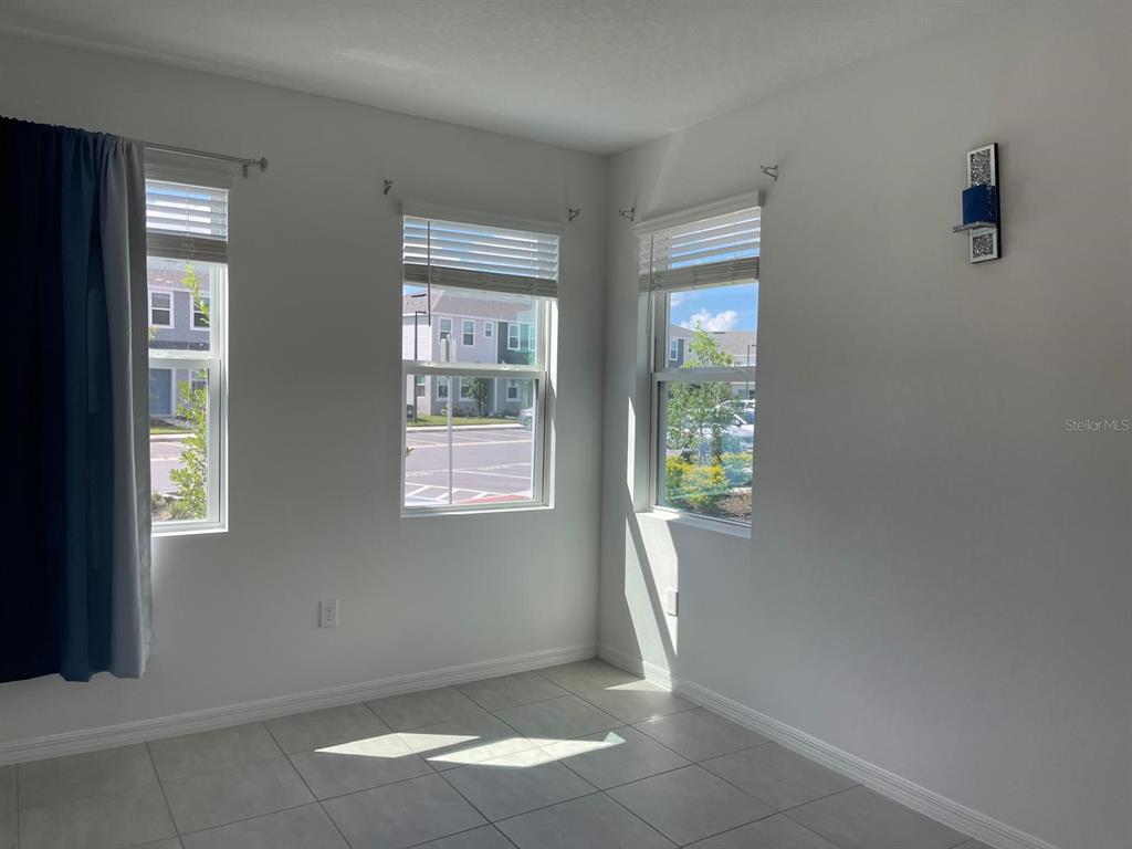 An empty room with light tile flooring, three windows with blinds, and white walls — 3335 COMPOSITION STREET, KISSIMMEE, FL
