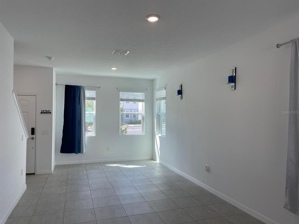An empty living room with white walls, tile flooring, and three windows with curtains — 3335 COMPOSITION STREET, KISSIMMEE, FL