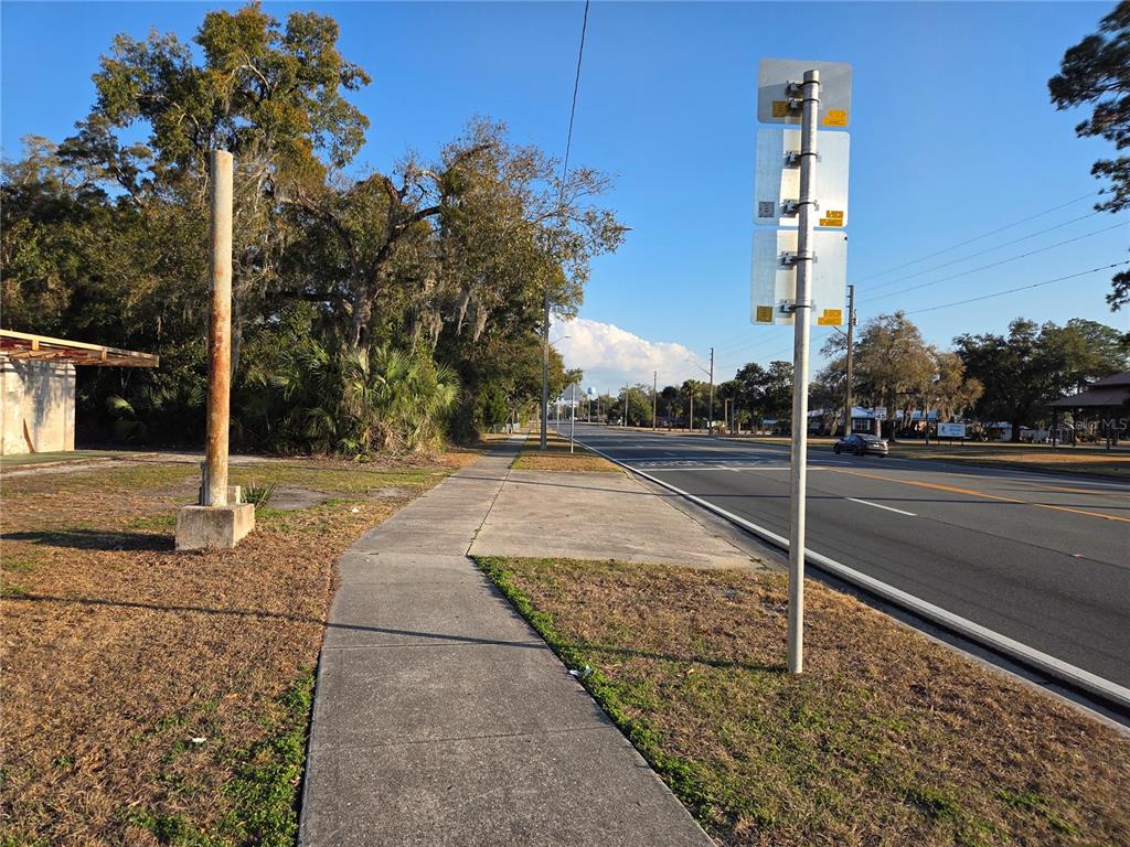 A sidewalk runs alongside a road with a metal signpost and trees in the background — 715 N YOUNG BOULEVARD, CHIEFLAND, FL