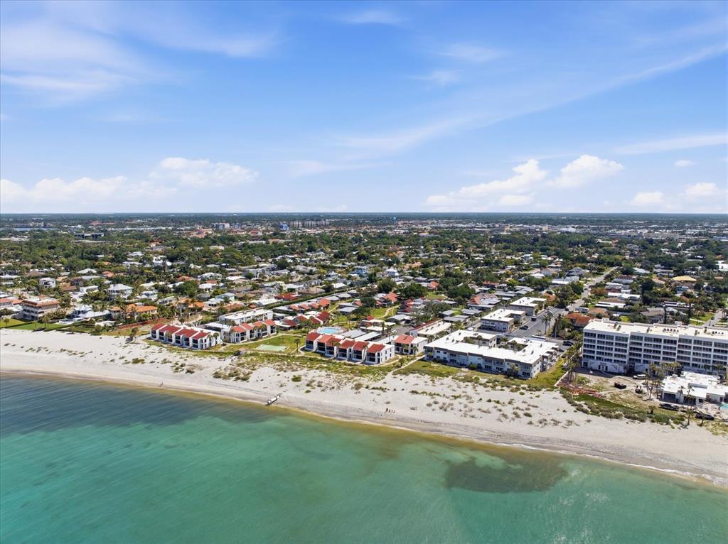 An aerial view shows beachfront apartment buildings along a sandy coastline with a residential neighborhood — 500 PARK BOULEVARD S UNIT 106, VENICE, FL