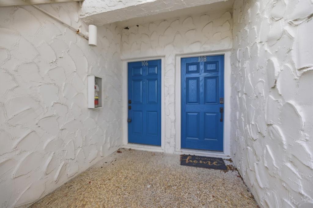 Two blue apartment doors labeled 106 and 108 are set in a textured white wall — 500 PARK BOULEVARD S UNIT 106, VENICE, FL