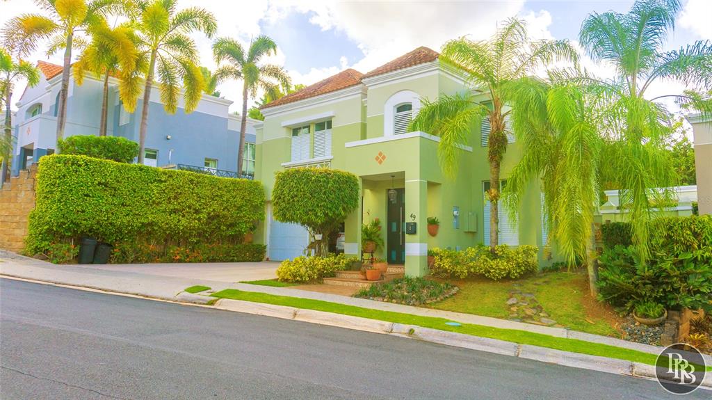 A two-story light green house with a paved driveway and palm trees in the front — 49 Vereda Street MONTEVERDE REAL DEV, SAN JUAN, PR
