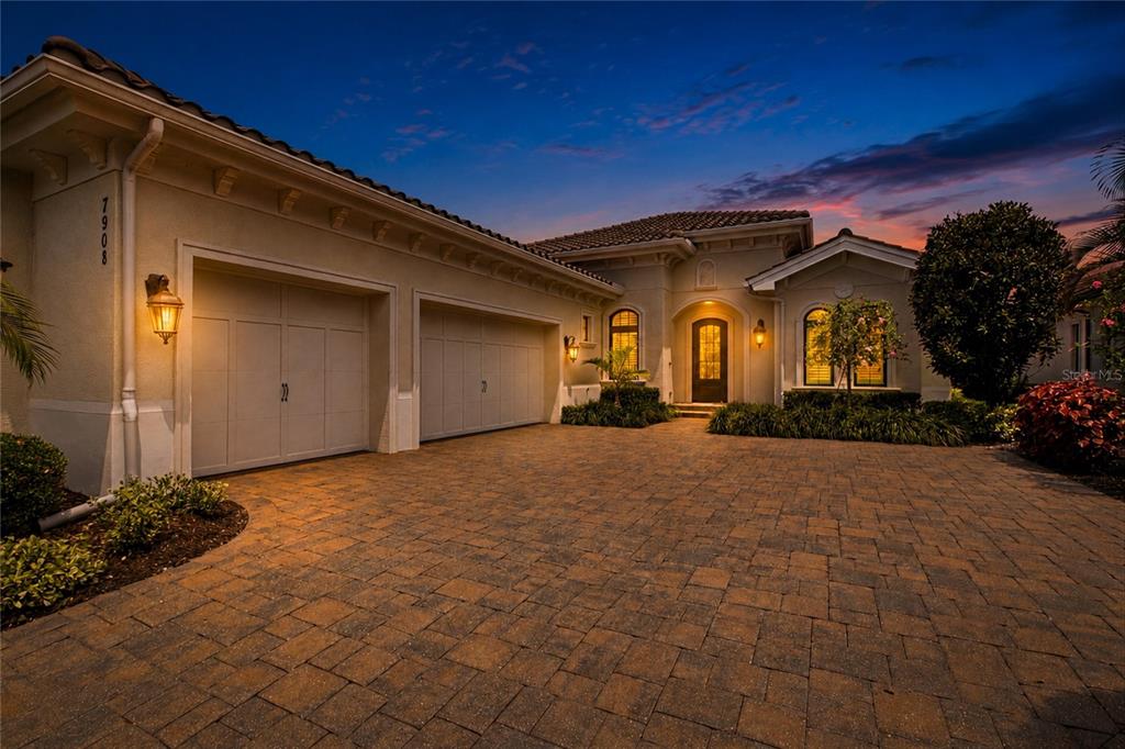 A single-story house exterior at dusk features a three-car garage and a paved driveway — 7908 MATERA COURT, BRADENTON, FL