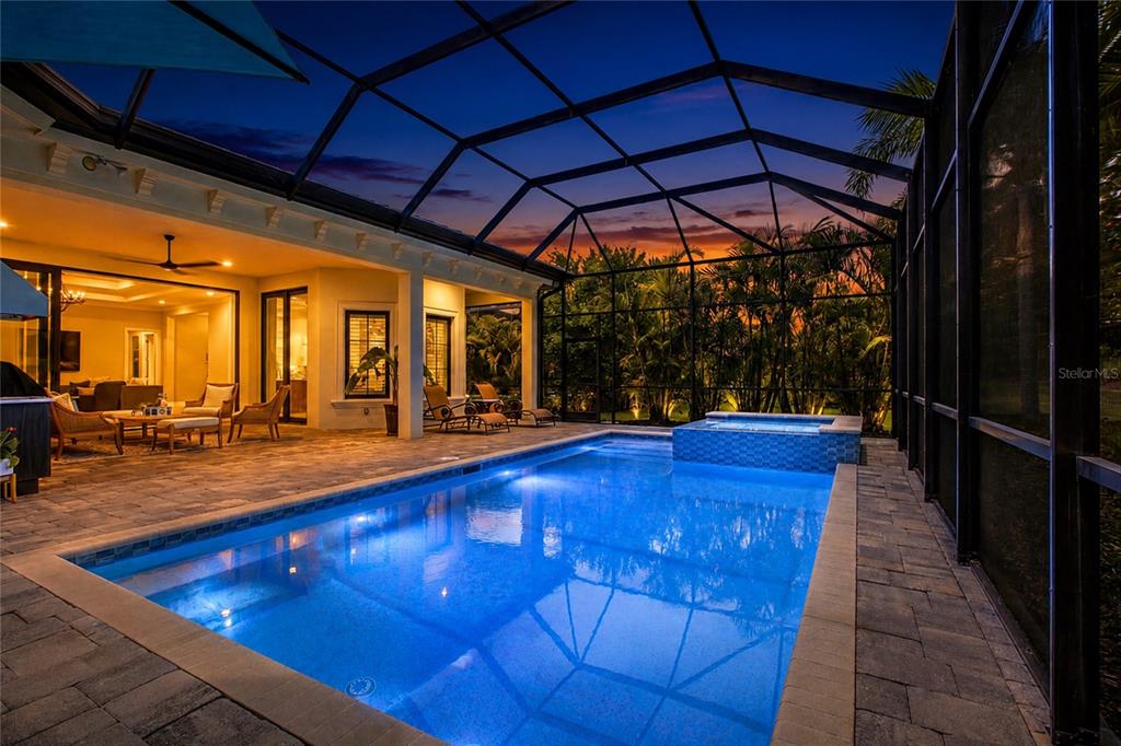 A swimming pool and hot tub are enclosed within a screened lanai at dusk — 7908 MATERA COURT, BRADENTON, FL