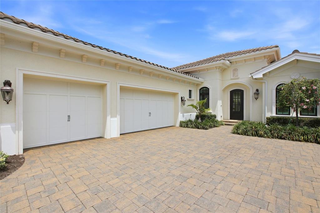 A beige house exterior features a two-car garage, a paved driveway, and a front entrance — 7908 MATERA COURT, BRADENTON, FL