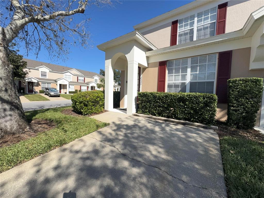 A concrete driveway leads to the covered entrance of a two-story townhouse with red shutters — 2333 SILVER PALM DRIVE, KISSIMMEE, FL