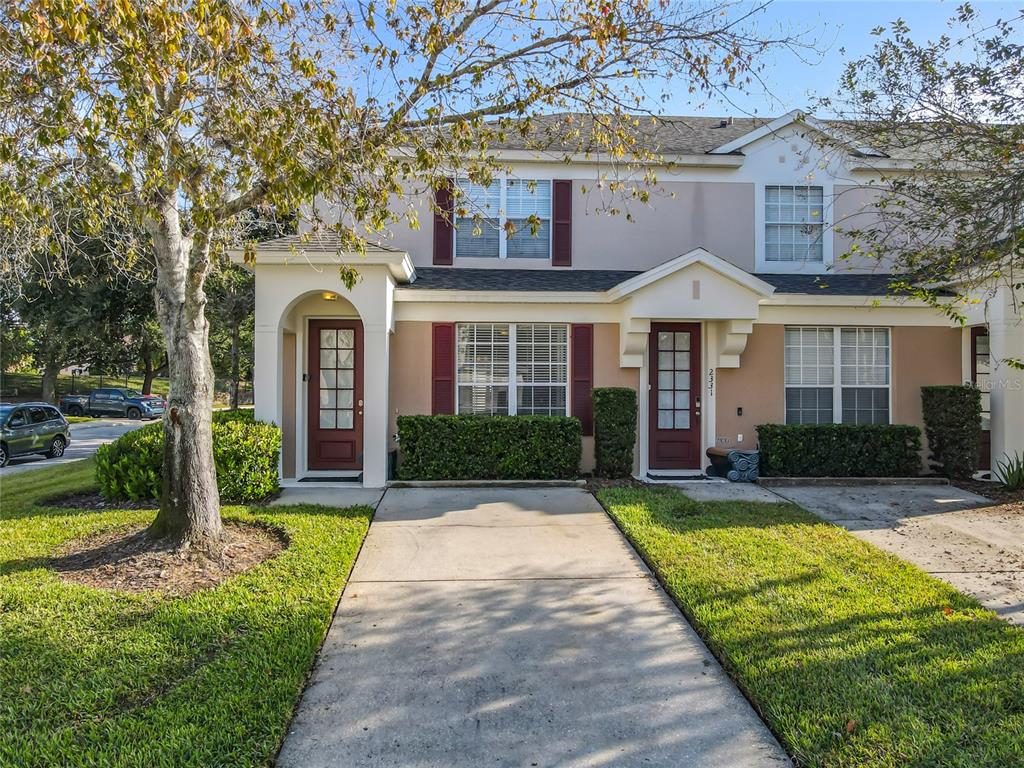A two-story townhouse exterior features a concrete driveway, maroon front doors, and manicured hedges — 2333 SILVER PALM DRIVE, KISSIMMEE, FL