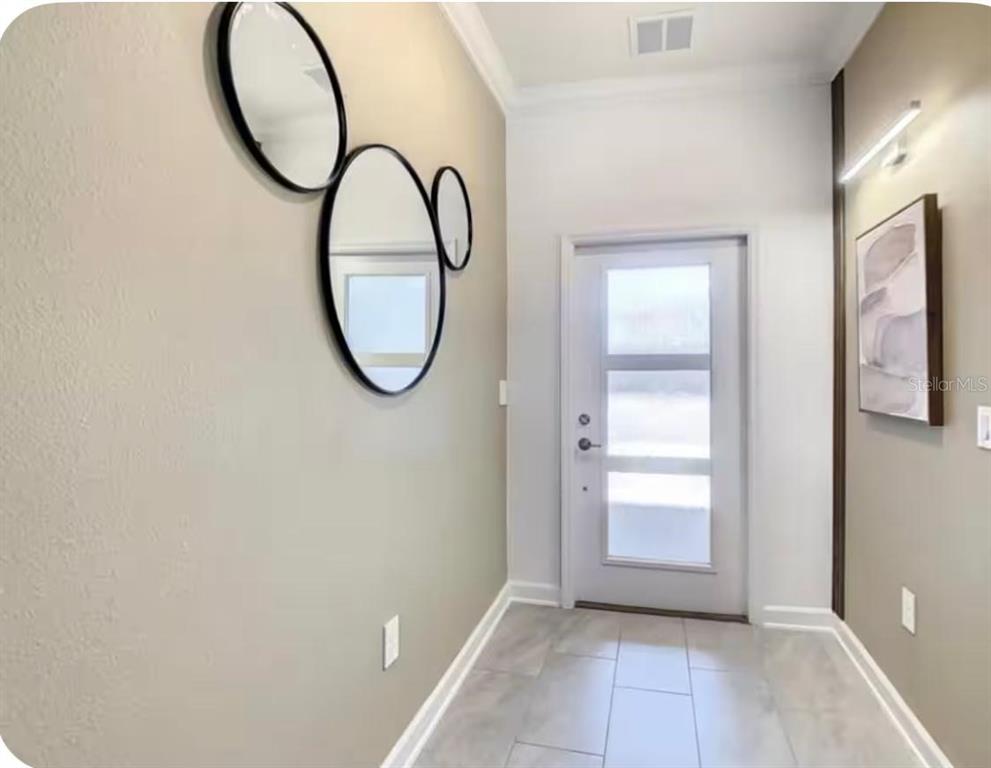 A modern entryway features light tile flooring, a white front door, and circular wall mirrors — 4479 SCENE LANE, KISSIMMEE, FL