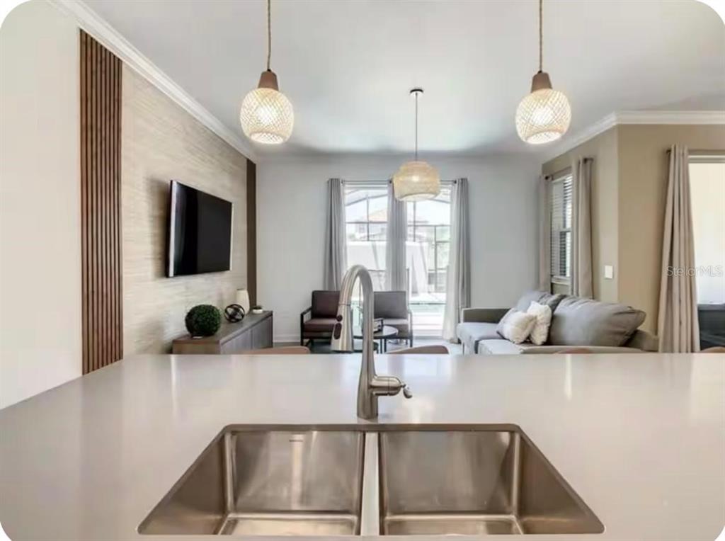A kitchen island with a stainless steel sink overlooks a living room with pendant lights — 4479 SCENE LANE, KISSIMMEE, FL