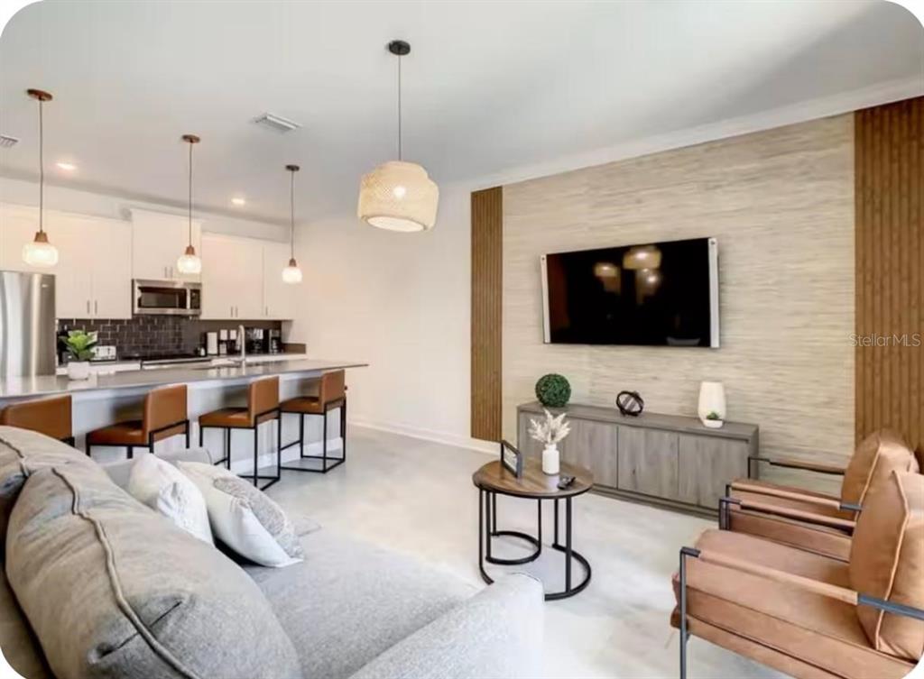 A modern open-concept living room and kitchen featuring a wall-mounted television and bar seating — 4479 SCENE LANE, KISSIMMEE, FL
