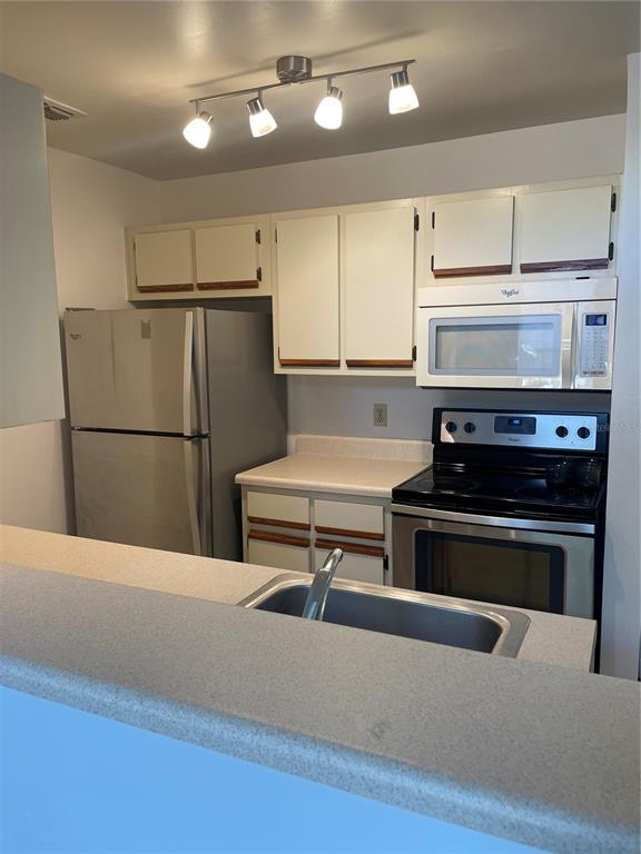 A kitchen features white cabinets, stainless steel appliances, and a gray countertop with a sink — 5992 WESTGATE DRIVE UNIT 302, ORLANDO, FL