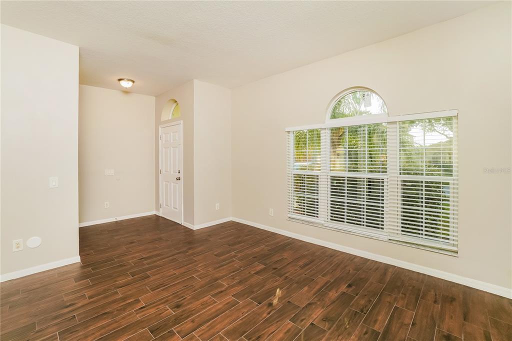 An empty room with wood-look tile flooring, beige walls, and a large arched window — 3610 BENERAID STREET, LAND O LAKES, FL