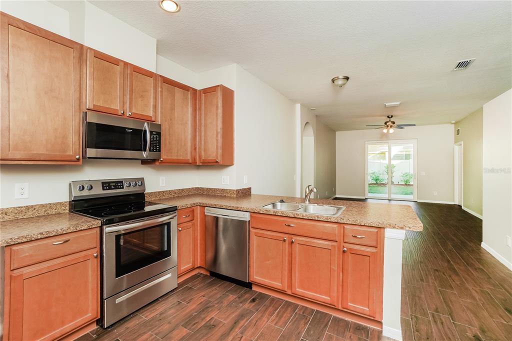 A kitchen with wood cabinets, stainless steel appliances, and granite countertops overlooks a living area — 3610 BENERAID STREET, LAND O LAKES, FL