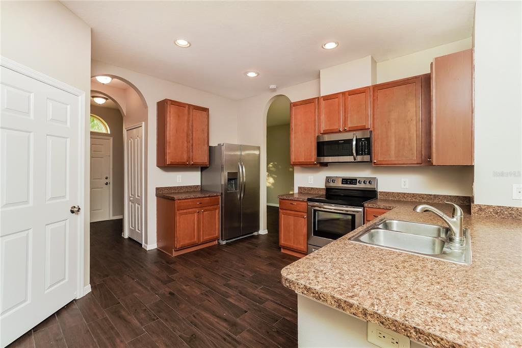 A kitchen with wood cabinets, stainless steel appliances, granite countertops, and dark wood-look flooring — 3610 BENERAID STREET, LAND O LAKES, FL