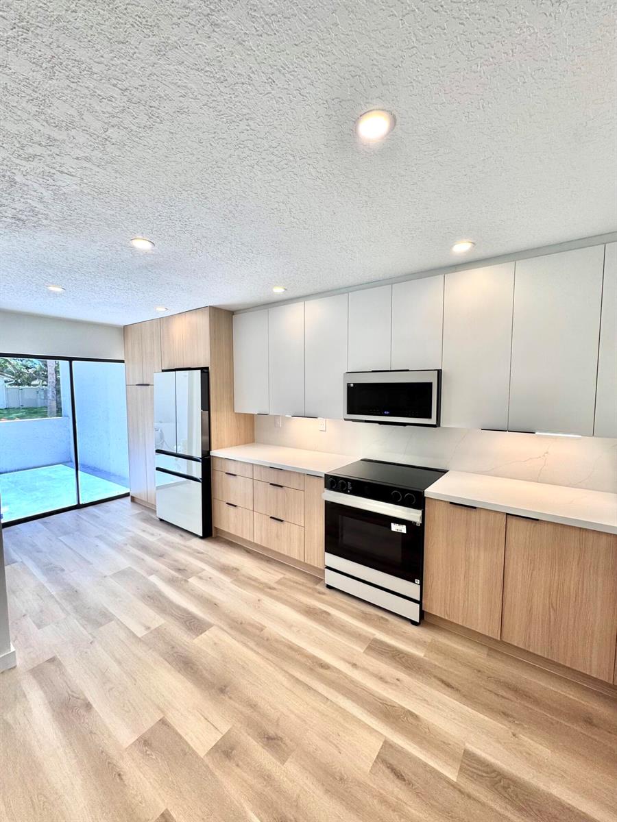 A modern kitchen features light wood cabinetry, white upper cabinets, stainless appliances, and wood flooring — 21547 Altamira Avenue, Boca Raton FL 33433, BOCA RATON, FL