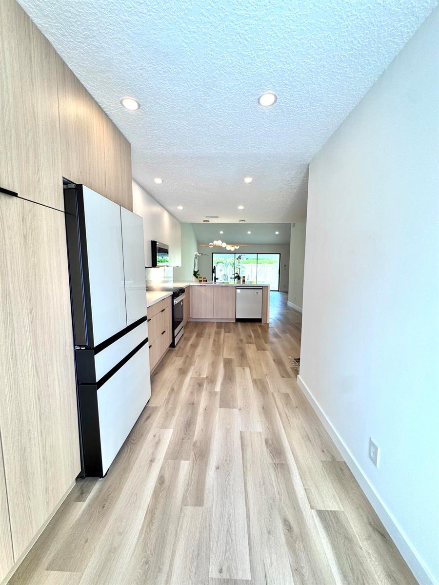 A modern kitchen features light wood cabinetry, stainless steel appliances, and wood-look flooring — 21547 Altamira Avenue, Boca Raton FL 33433, BOCA RATON, FL