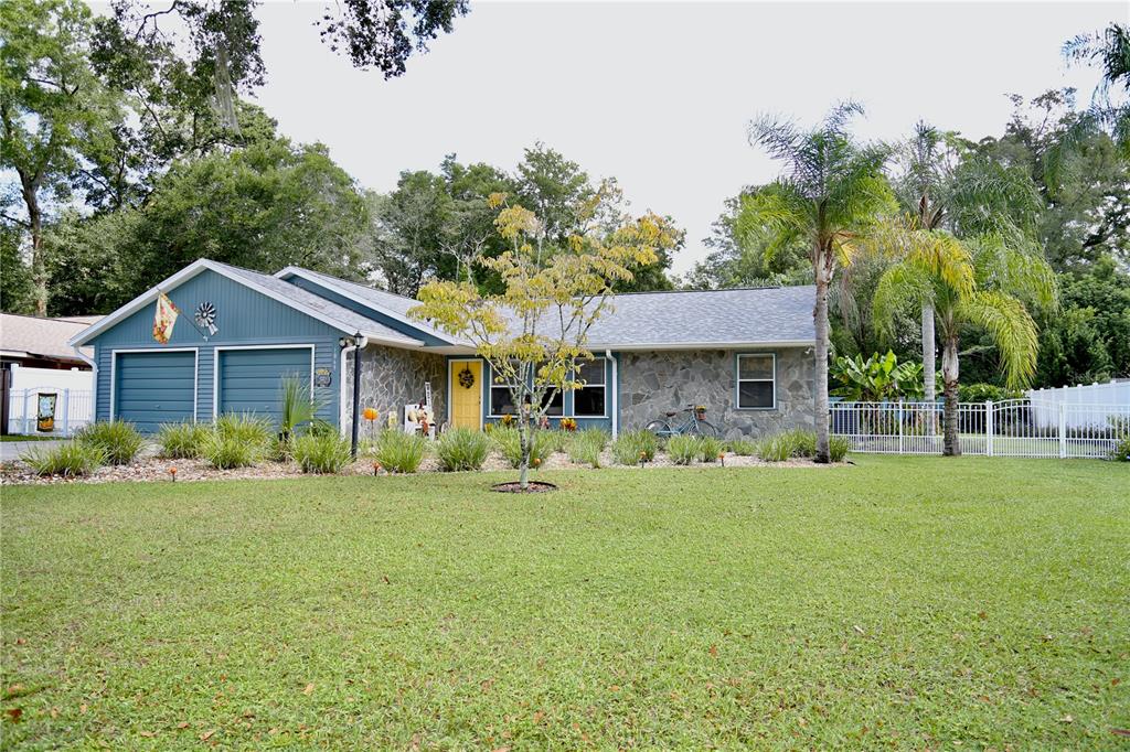 A blue house with a stone facade, yellow front door, and a large front lawn — 1069 SE 57TH AVENUE, OCALA, FL