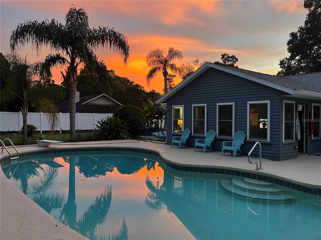 A swimming pool sits in front of a blue house under a vibrant sunset sky — 1069 SE 57TH AVENUE, OCALA, FL